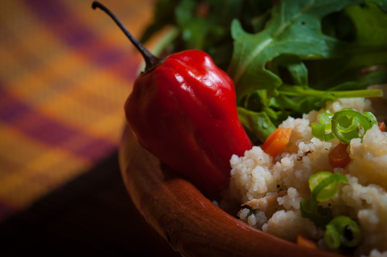 A bowl of spicy couscous garnished with fresh red pepper and rucola, creating a vibrant and healthy dish.